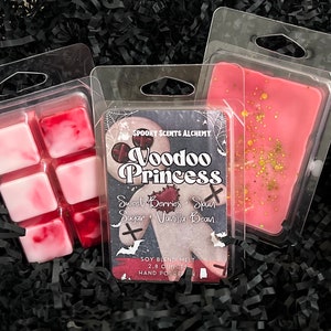 May include: Three wax melts in clear plastic containers. The wax melts are pink and white with a marbled effect. The container on the left has six squares of wax. The container on the right has one large square of wax. The container in the middle has a label that reads "SPOOKY SCENTS ALCHEMY Voodoo Princess Sweet Berries + Spun Sugar + Vanilla Bean SOY BLEND MELT 2.8 OUNCES HAND POURED".