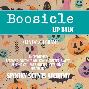 May include: A teal-colored label with the text "Boosicle LIP BALM" is set against a Halloween-themed background. The label also includes the size, ingredients, and the brand name "Spooky Scents Alchemy". The background features pumpkins, ghosts, and bats.