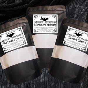 May include: Three matte black stand-up pouches containing laundry detergent. Each pouch features a white rectangular label with a black bat graphic and text reading Laundry Detergent, The Siren's Secret, Marauder's Midnight, or Haunted Tropics.