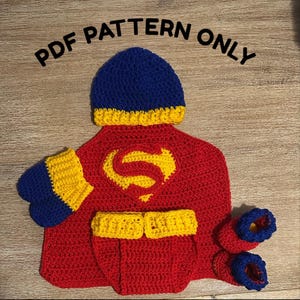 May include: A handmade crochet baby outfit in a Superman theme. The set includes a red cape with a yellow "S" emblem, a blue hat, yellow and blue cuffs, a diaper cover, and booties. The text "PDF PATTERN ONLY" is at the top.
