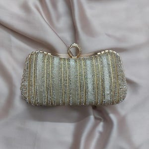 May include: A gold and silver clutch bag with a rhinestone design. The bag has a ring clasp.