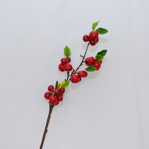 May include: A red berry branch with green leaves. The branch is made of brown wire and the berries are red and round.