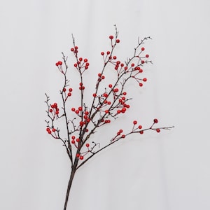 May include: A single artificial branch with dark brown stems and numerous small, bright red berries. The berries are clustered along the delicate branches, creating a visually striking contrast against the white background. Ideal for seasonal decor.