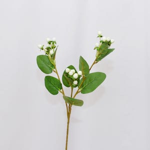 Może przedstawiać: Sztuczna łodyga z zielonymi liśćmi i małymi skupiskami białych jagód. Łodyga jest w kolorze jasnobrązowym, a liście są w żywym zielonym kolorze. Jagody są małe i okrągłe, dodając delikatnego akcentu.