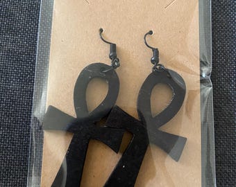 May include: A pair of black wooden earrings shaped like the Ankh symbol. The earrings are hanging from a brown card.
