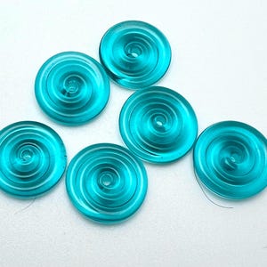 May include: Six teal blue glass buttons with a spiral design. The buttons are round and have a hole in the center.