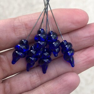 K&ouml;nnte beinhalten: Ein Satz von sieben kobaltblauen Glasperlen, jede mit einem einzigartigen Spiraldesign, sind auf d&uuml;nnen Silberdr&auml;hten aufgef&auml;delt. Die Perlen sind etwa 2,5 cm lang.