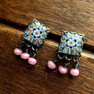 May include: A pair of earrings with a blue and gold tile design and pink beads hanging from the bottom. The tile design features a floral pattern.