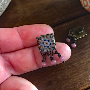 May include: A pair of earrings with a blue and white patterned tile design and pink beads hanging from the bottom.