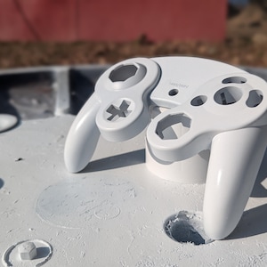 Puede incluir: Una carcasa de mando de videojuegos en color blanco sólido con un acabado liso y brillante. La carcasa incluye aberturas para los joysticks, la cruceta y los botones de acción, con el logotipo de Nintendo grabado en la parte central.