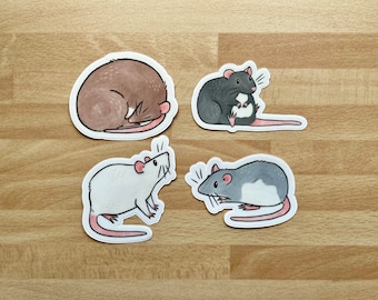 Könnte beinhalten: Vier illustrierte Ratten-Aufkleber auf einem Holzgrund. Die Aufkleber sind weiß, grau, braun und schwarz. Die Ratten sind in verschiedenen Posen, darunter schlafend, sitzend und stehend.