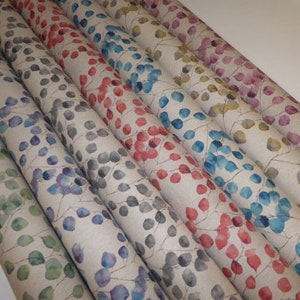 May include: Close-up of fabric rolls with a watercolour leaf pattern in various colours, including green, blue, purple, red, and gold. The fabric has a natural linen texture.