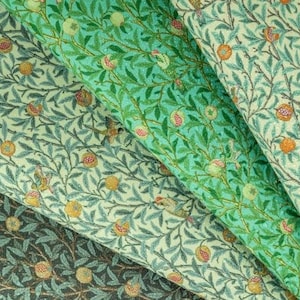 May include: Three fabric swatches with a repeating pattern of green leaves, small white flowers, and red pomegranates. The fabric is a light green, a light beige, and a dark green.