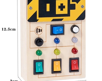 Puede incluir: Un panel de control de juguete de madera con un símbolo de batería amarillo y negro, un interruptor azul, una perilla negra y varias luces y interruptores de colores. El panel mide 12,5 cm de alto, 8,2 cm de ancho y 3 cm de profundidad.