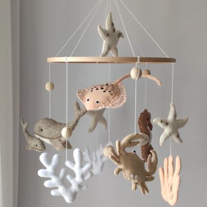 May include: A wooden mobile with felt sea creatures, including a whale, stingray, starfish, crab, seahorse, and coral. The mobile is suspended from a wooden ring.