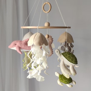 A baby mobile in a nautical boho style for a crib with felt sea creatures: jellyfish, dolphin, turtle, and seahorse in neutral colors.
