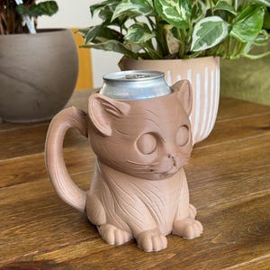 May include: A brown ceramic cat mug with a handle, holding a silver can with the text "Zero Calories".