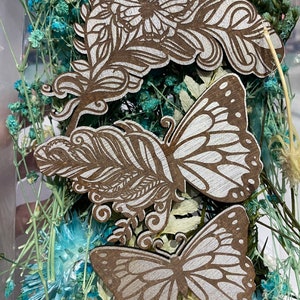 Peut inclure: Trois motifs de papillons et de fleurs en bois avec une finition peinte blanche. Les motifs sont sur un fond de fleurs séchées bleues et blanches.