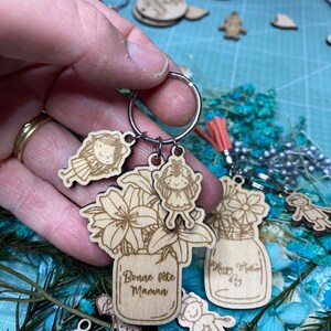 Peut inclure: Porte-clés en bois avec un pot de fleurs et le texte "Bonne fête Maman". Le porte-clés comprend également deux petites figurines en bois d'enfants.