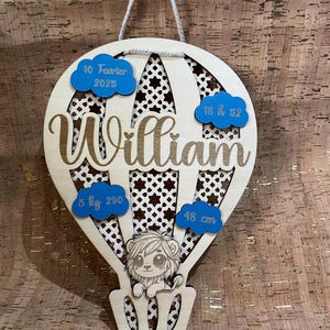 Peut inclure: Annonce de naissance en bois en forme de ballon à air chaud avec des nuages bleus et un lion. Les nuages comportent les textes suivants : "10 Januar 2023", "18 h 52", "3 kg 290" et "48 cm". Le ballon porte le nom "William".