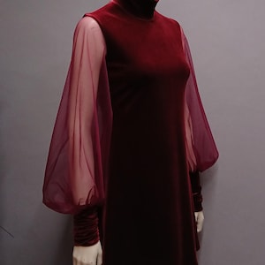 May include: A deep burgundy velvet dress featuring a high mock neck and long, voluminous sheer organza sleeves. The sleeves are gathered at the wrists with wide velvet cuffs, creating a distinct contrast between the opaque bodice and the translucent fabric.