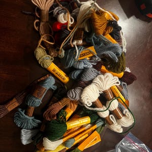 May include: A pile of colorful embroidery floss spools in various shades of blue, green, brown, yellow, red, and white. The spools are labeled "DMC" and "Patons".