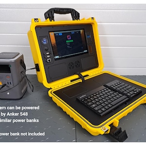 May include: A yellow portable computer system with a black keyboard and screen. The system is open, revealing the screen and keyboard. A gray Anker power bank is to the left. Text on the image reads: System can be powered by Anker 548 or similar power banks.