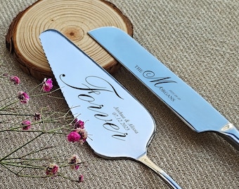 May include: Silver cake server and knife set. The server has the word "Forever" in script, along with names and a date. The knife is engraved with "The Morgans" and a date. Pink flowers and a wood slice are in the background.