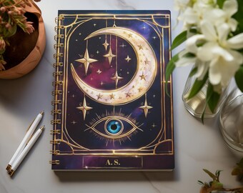 May include: A dark purple notebook with a gold frame and a crescent moon with stars and an eye design. The notebook has a gold spiral binding and the initials "A.S." printed on the front.