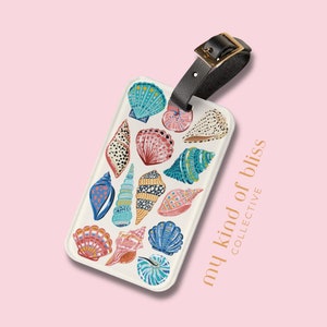 May include: Luggage tag with a collection of colorful seashells in shades of blue, pink, and teal on a white background. The tag has a black leather strap with a gold buckle. The text "my kind of bliss collective" is printed on the tag.