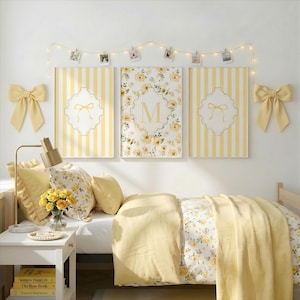 May include: A bedroom decorated in yellow and white. The bed features a floral duvet and pillows. Above the bed are three framed artworks: two with yellow stripes and one with a floral design and the letter "M". The room is decorated with yellow bows and fairy lights.