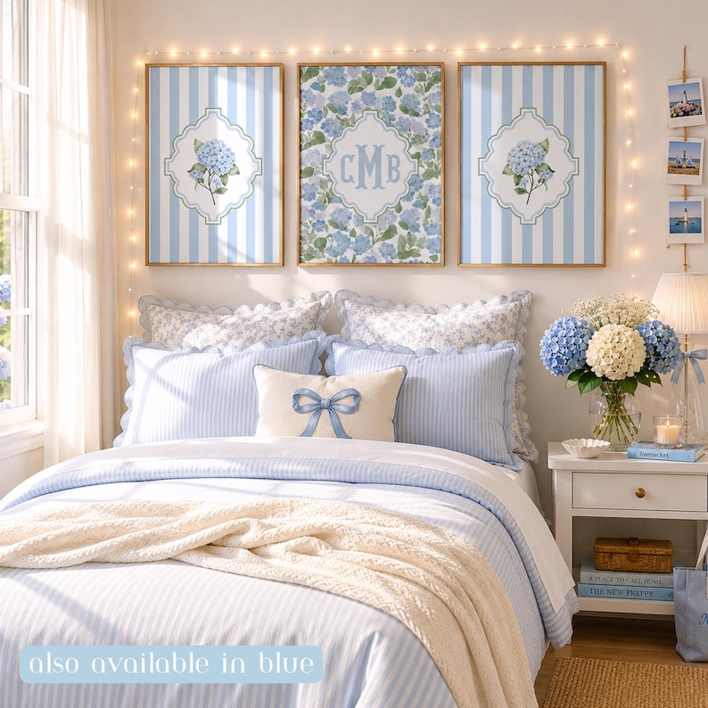 Op de afbeelding: Een slaapkamer met drie ingelijste kunstwerken met blauw-witte strepen en hortensiamotieven, inclusief een centrale print met monogram. Het bed heeft blauw gestreept beddengoed, een cr&egrave;mekleurige plaid en een kussen met een blauwe strik.