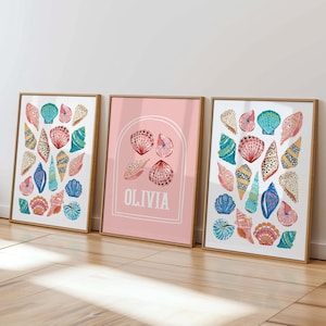May include: Three framed art prints with colourful seashell illustrations. The prints display various shells in shades of blue, pink, and yellow against a white backdrop. One print features the name "OLIVIA" on a pink background.