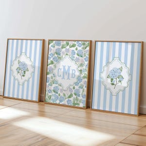 May include: Three framed wall art pieces. Two feature blue and white striped backgrounds with a floral emblem and a hydrangea. The third has a floral pattern with the letters "CMB" in a white emblem.