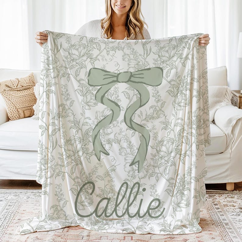 My Personalized Sage Green Bow Toile Name Blanket features a classic olive toile print with delicate flowers and birds on a crisp white background, topped with a big coquette-style bow and your custom name in an elegant script below. Soft feminine and beautifully detailed, it’s perfect for babies, kids, teens and adults. Great for sleepover favors, hospital or coming-home blankets, announcement photos, dorm rooms, teen bedrooms, Christmas, birthdays, sisters, newborn keepsakes and new parents