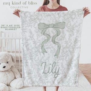 My Personalized Sage Green Bow Toile Name Blanket features a classic olive toile print with delicate flowers and birds on a crisp white background, topped with a big coquette-style bow and your custom name in an elegant script below. Soft feminine and beautifully detailed, it’s perfect for babies, kids, teens and adults. Great for sleepover favors, hospital or coming-home blankets, announcement photos, dorm rooms, teen bedrooms, Christmas, birthdays, sisters, newborn keepsakes and new parents