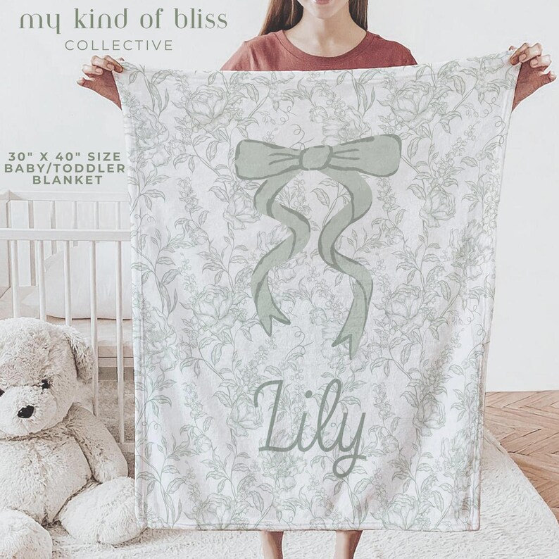 My Personalized Sage Green Bow Toile Name Blanket features a classic olive toile print with delicate flowers and birds on a crisp white background, topped with a big coquette-style bow and your custom name in an elegant script below. Soft feminine and beautifully detailed, it’s perfect for babies, kids, teens and adults. Great for sleepover favors, hospital or coming-home blankets, announcement photos, dorm rooms, teen bedrooms, Christmas, birthdays, sisters, newborn keepsakes and new parents