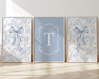 May include: Three framed prints with a light blue and white floral pattern. Two prints feature a blue bow, while the center print has a light blue background with the letter "T" in white. The frames have a gold color.