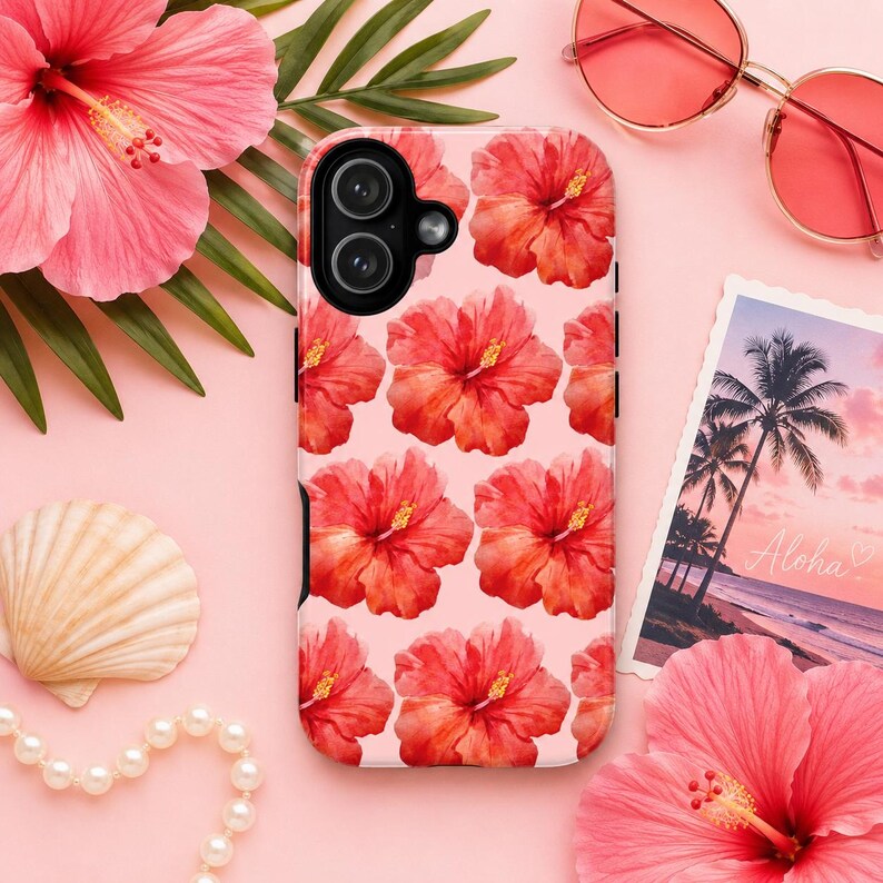 Pink hibiscus floral phone case displayed in a tropical flat lay with oversized hibiscus flowers, palm leaves, pearl bracelet, seashell, and pink sunglasses. Feminine summer aesthetic iPhone case with watercolor hibiscus pattern on a soft blush pink background, perfect for tropical vacations, beach lovers, Hawaii trips, and coquette-inspired phone accessories.