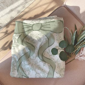My Personalized Sage Green Bow Toile Name Blanket features a classic olive toile print with delicate flowers and birds on a crisp white background, topped with a big coquette-style bow and your custom name in an elegant script below. Soft feminine and beautifully detailed, it’s perfect for babies, kids, teens and adults. Great for sleepover favors, hospital or coming-home blankets, announcement photos, dorm rooms, teen bedrooms, Christmas, birthdays, sisters, newborn keepsakes and new parents