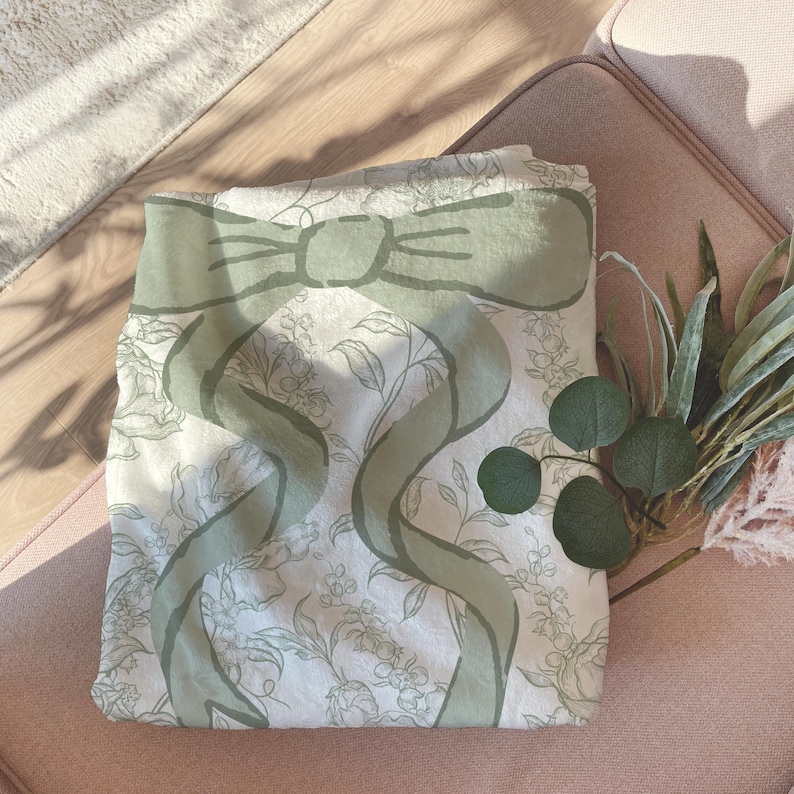 My Personalized Sage Green Bow Toile Name Blanket features a classic olive toile print with delicate flowers and birds on a crisp white background, topped with a big coquette-style bow and your custom name in an elegant script below. Soft feminine and beautifully detailed, it’s perfect for babies, kids, teens and adults. Great for sleepover favors, hospital or coming-home blankets, announcement photos, dorm rooms, teen bedrooms, Christmas, birthdays, sisters, newborn keepsakes and new parents