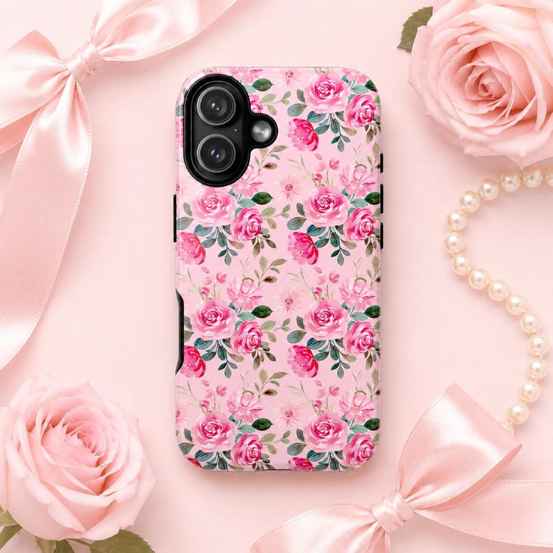 Pink floral phone case with watercolor roses displayed on a soft blush pink background. Styled with satin ribbon bows, pink roses, and pearl accents for a feminine coquette aesthetic. Cute girly iPhone case featuring an all-over floral pattern, perfect for teen girls, pink lovers, and cottagecore-inspired accessories.