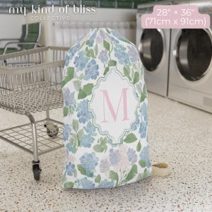 Large personalized floral laundry bag with pink monogram initial beside washing machines, college dorm laundry storage bag