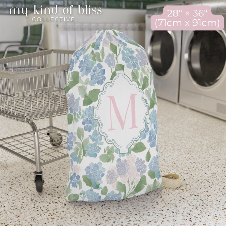 Large personalized floral laundry bag with pink monogram initial beside washing machines, college dorm laundry storage bag