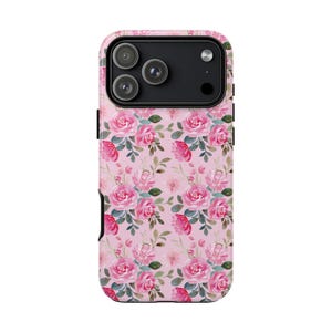 Pu&ograve; includere: Una custodia per smartphone con un motivo ripetuto di rose rosa e foglie verdi su sfondo rosa chiaro. La custodia presenta un ritaglio nero per il modulo fotocamera nella parte superiore, che rivela tre lenti circolari e un flash del dispositivo.
