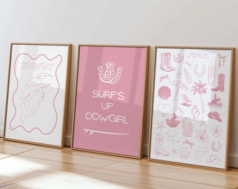 May include: Three framed art prints with a western and beach theme. The left print says "HOWDY" with a cowgirl illustration. The center print is pink with "SURF'S UP COWGIRL" text. The right print has various cowgirl and beach icons.