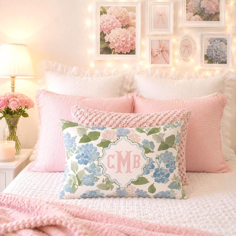 Custom hydrangea monogram pillow on a cozy feminine bed with blush pink bedding, white textured pillows, and coquette wall art.
