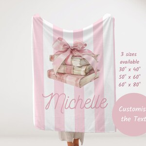 My Custom Name Book Lover Coquette Blanket. Featuring a pink and white striped background with a watercolor book stack wrapped in a bow, this plush blanket is as cozy as it is cute. Add your custom name underneath for a personalized, preppy, coquette touch. Perfect for book lovers, girls bedrooms, baby showers, newborns, or a stylish preppy touch to dorm