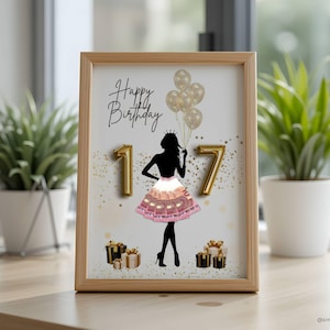 May include: A framed print with a light wood frame. The print features a black silhouette of a person wearing a crown and holding balloons. The words "Happy Birthday" are written above the silhouette, with the numbers "17" in gold. Gold confetti and gift boxes are also included.