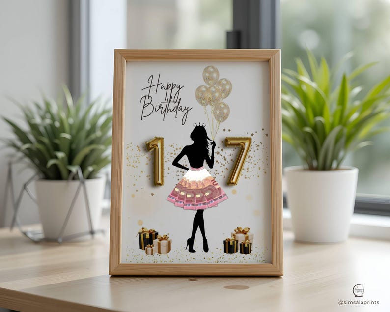 May include: A framed print with a light wood frame. The print features a black silhouette of a person wearing a crown and holding balloons. The words "Happy Birthday" are written above the silhouette, with the numbers "17" in gold. Gold confetti and gift boxes are also included.